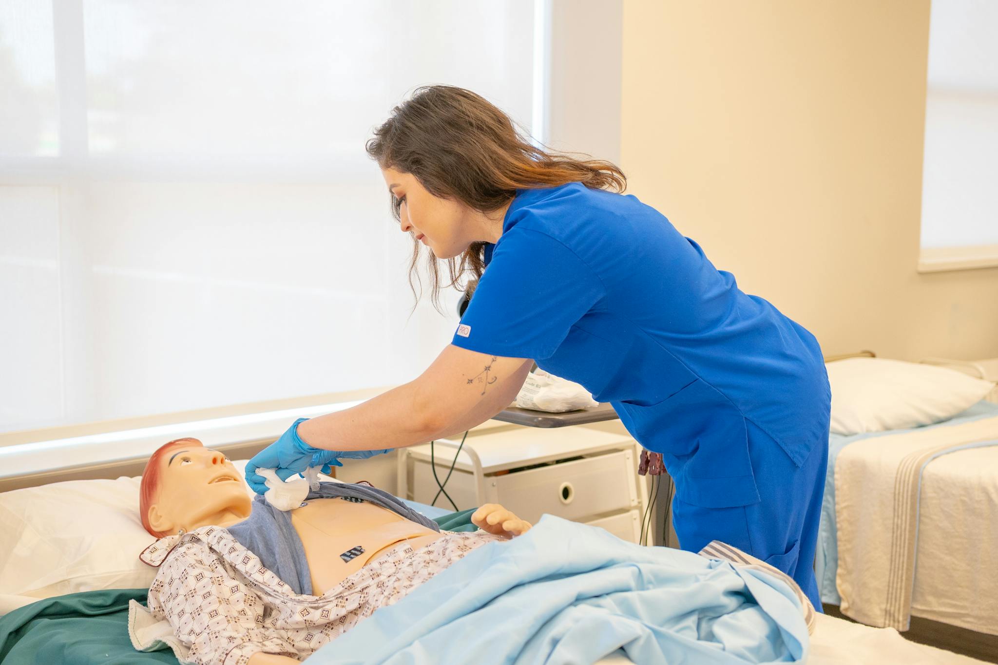 A nurse in blue scrubs trains on a medical dummy in a healthcare facility.